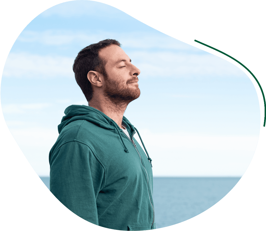 A man with his eyes closed and he is standing by the ocean.